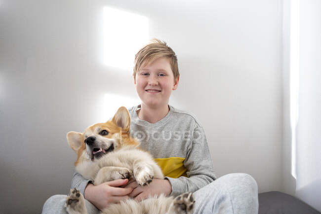 Portrait of boy sitting on bed at home cuddling his dog — Stock Photo