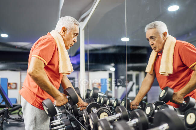 Hombre mayor tomando pesas de estante en el gimnasio - foto de stock