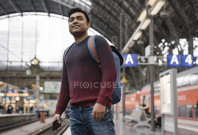 Hombre con smartphone esperando el tren en la estación de tren - foto de stock