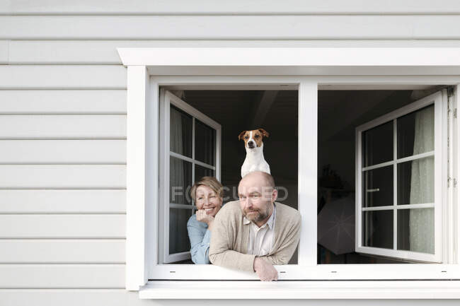 Couple with dog leaning out of window of their house — Stock Photo