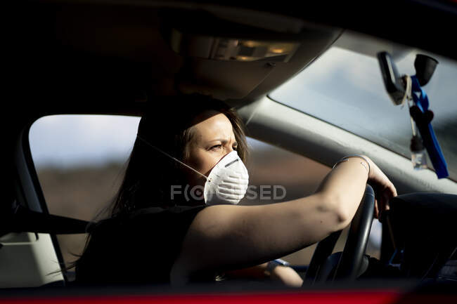 Женщина в машине в маске респиратора — стоковое фото