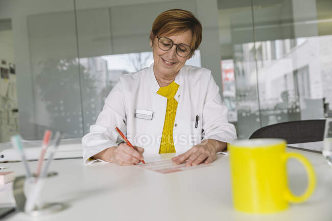 Médico sentado na mesa a preencher a prescrição — Fotografia de Stock