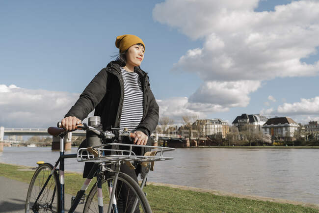 Mujer con bicicleta en la orilla del río, Frankfurt, Alemania - foto de stock