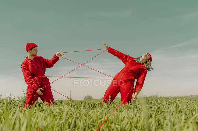 Молодая пара в красных комбинезонах и шляпах выступает на поле с красной ниткой — стоковое фото
