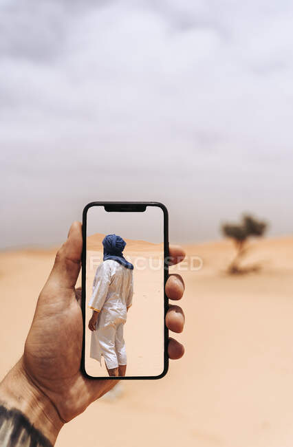 Рука тримає смартфон з фото людини, що йде в пустелі — стокове фото