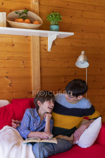 Bonne mère et fille lisant un livre sur canapé dans une cabane en bois — Photo de stock