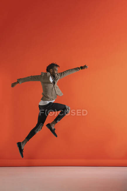 Молодой человек прыгает и танцует перед оранжевой стеной — стоковое фото