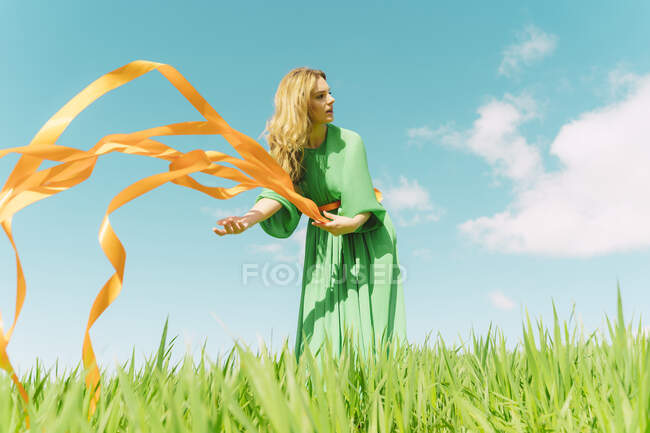 Giovane donna che indossa un abito verde in piedi in un campo con nastri soffianti — Foto stock