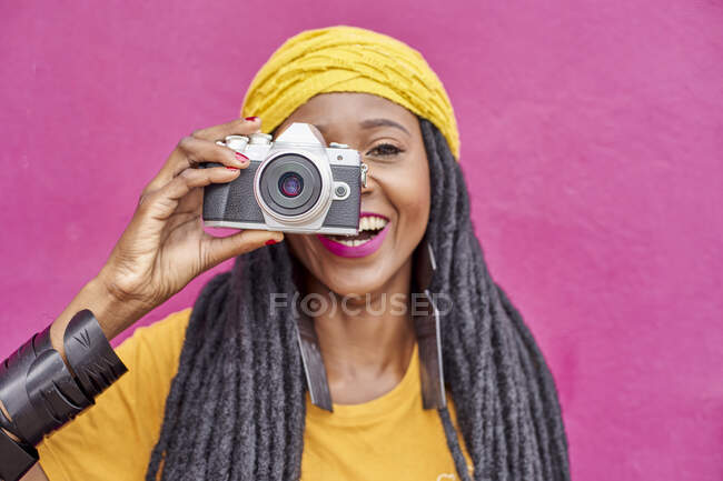 Портрет женщины с длинными дредами и фотоаппаратом в стиле ретро перед розовой стеной — стоковое фото