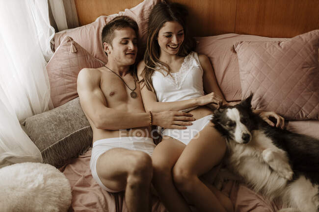 Счастливая молодая пара и собака лежат в постели — стоковое фото