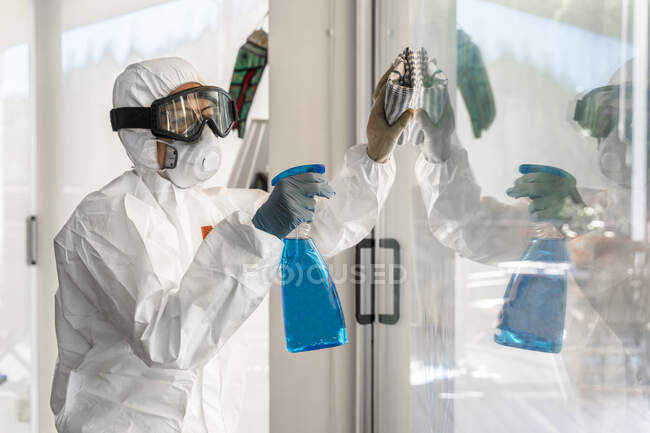 Mujer con ropa protectora, desinfectando su casa, limpiando ventanas - foto de stock