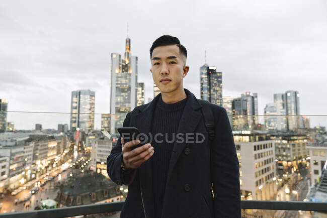 Porträt eines Mannes, der in der Abenddämmerung sein Smartphone in der Stadt hält — Stockfoto