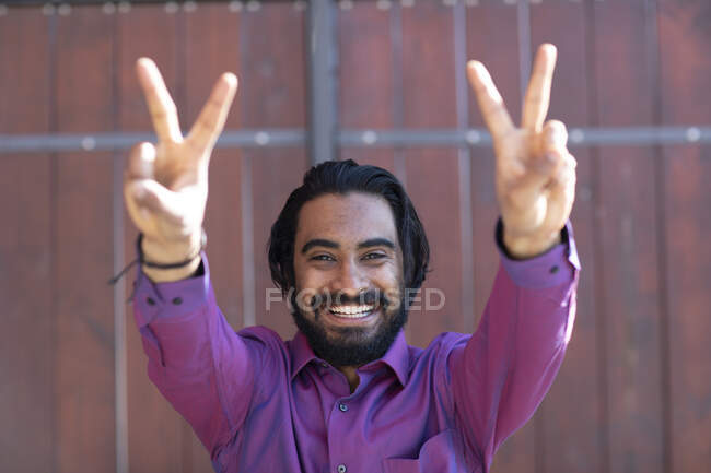 Молодой улыбающийся человек делает знак мира перед воротами — стоковое фото