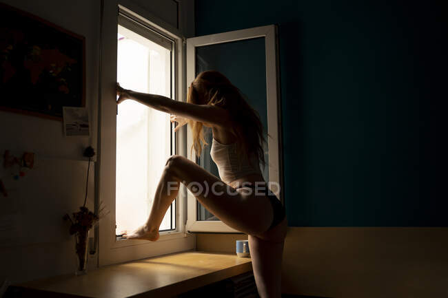 Mujer joven en casa subiendo por la ventana - foto de stock