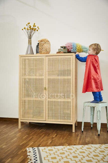 Хлопчик у костюмі Супермена і прибирання іграшки з пір'ям на буфеті вдома — стокове фото