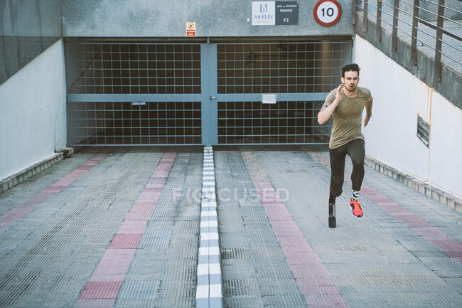 Atleta discapacitado con prótesis de pierna corriendo por la rampa en un garaje - foto de stock