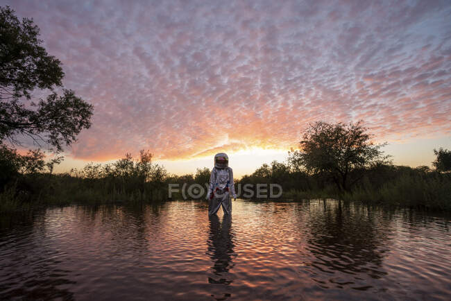 Spacewoman standing in water at sunset — Stock Photo