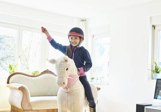 Girl riding on play horse at home — Stock Photo