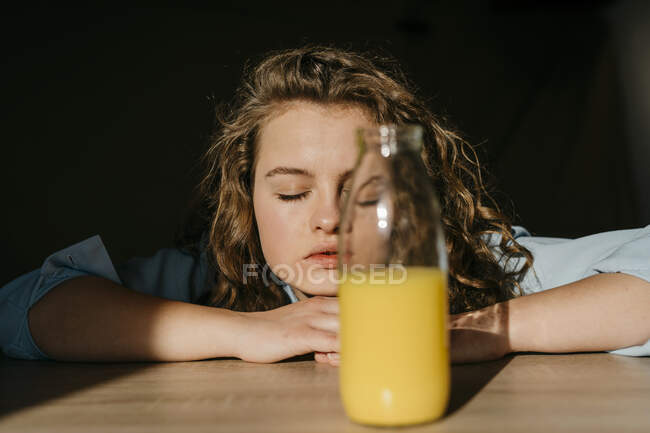 Retrato de una joven rubia con los ojos cerrados apoyados en la mesa - foto de stock