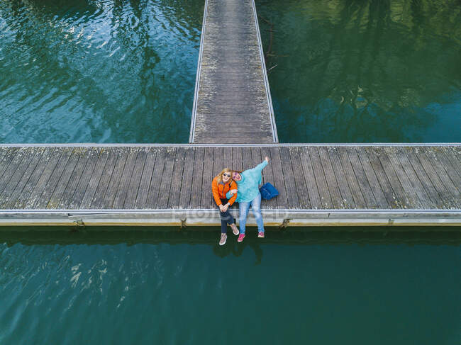 Two happy friends sitting side by side on jetty, Valdemurio Reservoir, Asturias, Spain — Stock Photo