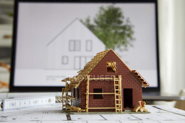 Architecture, model of home ownership on construction plan, laptop in the background — Stock Photo