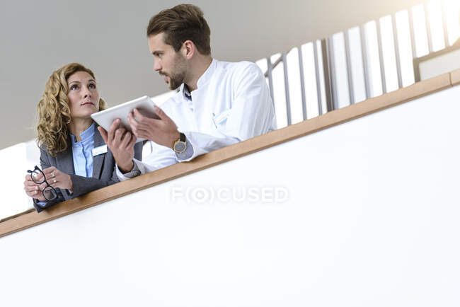 Femme d'affaires et médecin avec comprimé parlant à l'hôpital — Photo de stock
