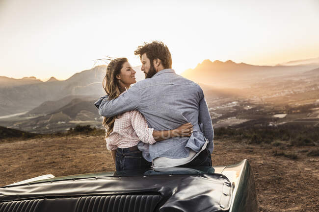 Couple affectueux en voiture convertible à la campagne au coucher du soleil — Photo de stock