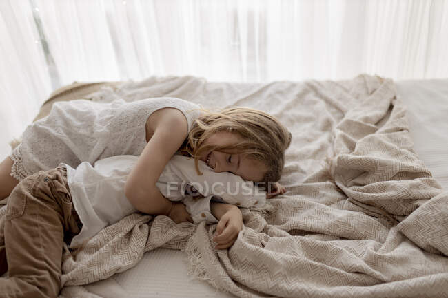 Souriante petite fille allongée sur le lit câlinant son frère — Photo de stock