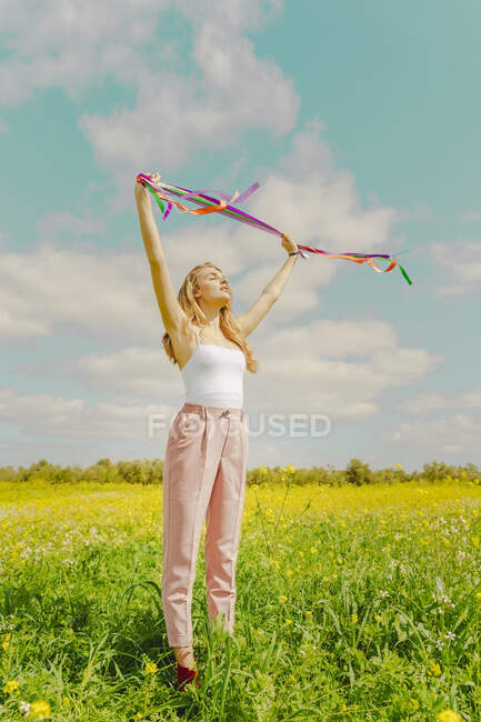 Mujer joven con cintas de colores en un prado de flores en primavera - foto de stock