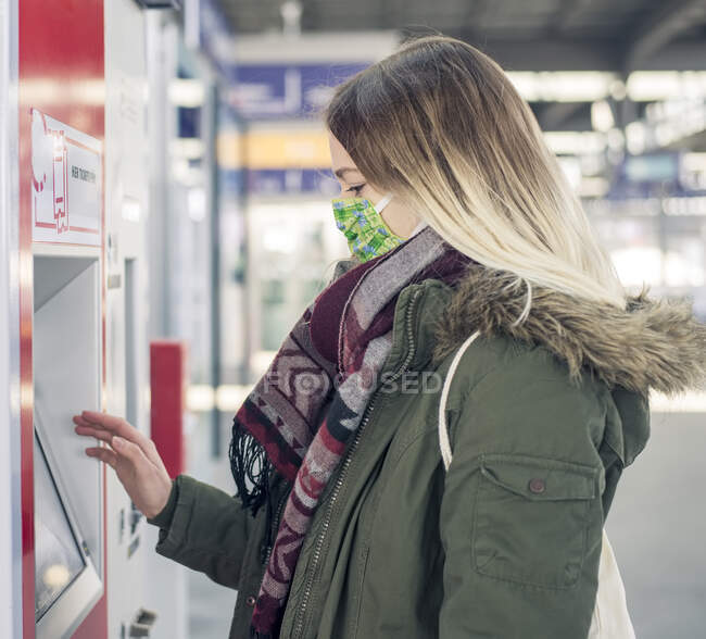 Jeune femme portant un masque à l'aide d'un distributeur de billets à la gare — Photo de stock