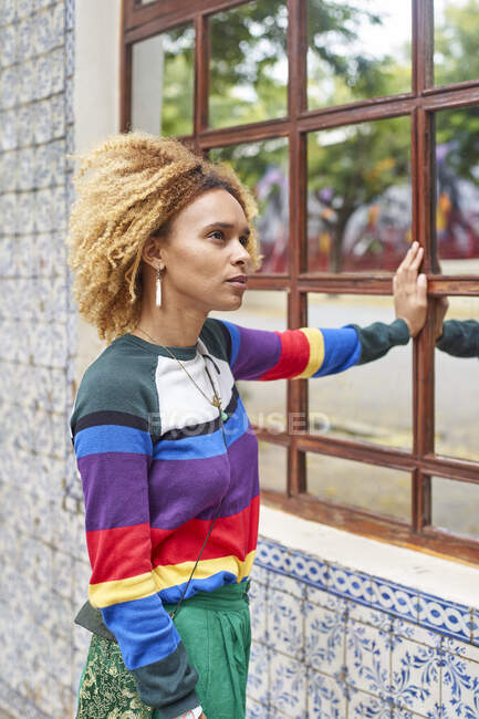 Portrait of a young womanwith an afro hairstyle leaning on a mirrored window — Stock Photo