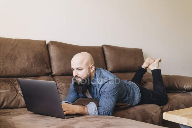 Uomo d'affari che utilizza il computer portatile mentre si trova sul divano in soggiorno a casa — Foto stock