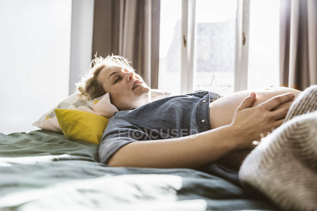 Pregnant woman lying on bed at home touching her belly — Stock Photo