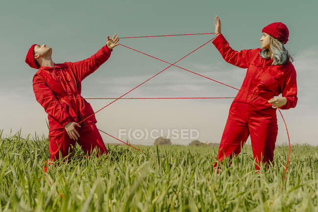 Jeune couple portant des salopettes rouges et des chapeaux se produisant sur un terrain avec une ficelle rouge — Photo de stock