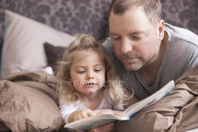 Padre e figlia che leggono un libro a letto — Foto stock