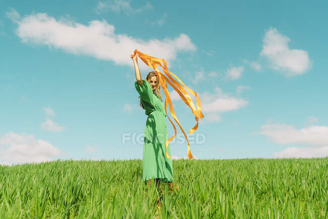 Felice giovane donna che indossa un vestito verde in un campo con nastri soffianti — Foto stock