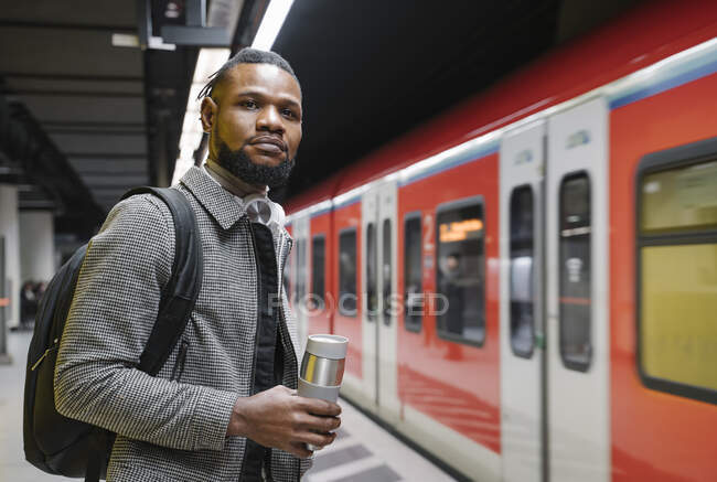 Elegante hombre con copa reutilizable y auriculares en una estación de metro - foto de stock