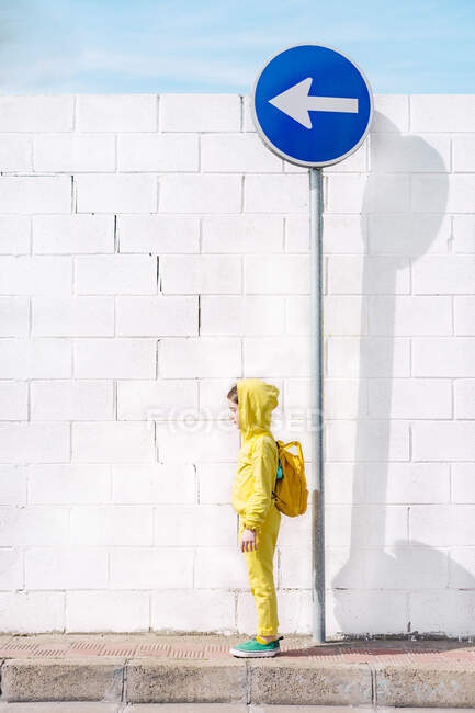 Mädchen steht auf einem Verkehrsschild, Richtung links, vor einer weißen Wand — Stockfoto