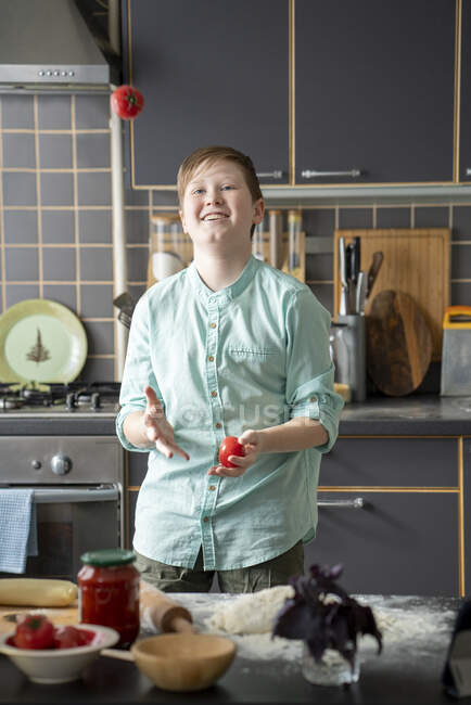 Portrait of smiling boy juggling with tomatoes in the kitchen — Stock Photo