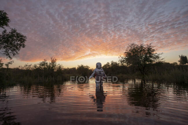 Spacewoman walking in water at sunset — Stock Photo