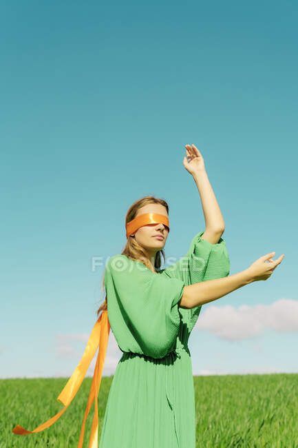 Blindfolded young woman wearing a green dress standing in a field — Stock Photo