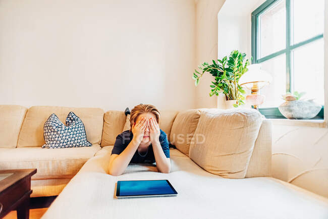 Boy lying on couch in living room at home covering his eyes — Stock Photo