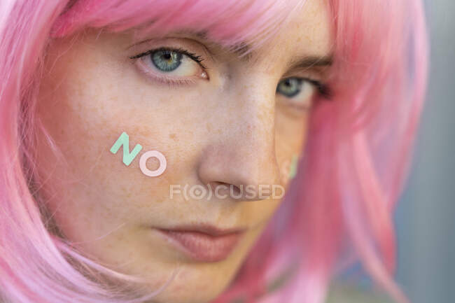 Retrato de jovem mulher usando peruca rosa com palavra 'não' na bochecha — Fotografia de Stock