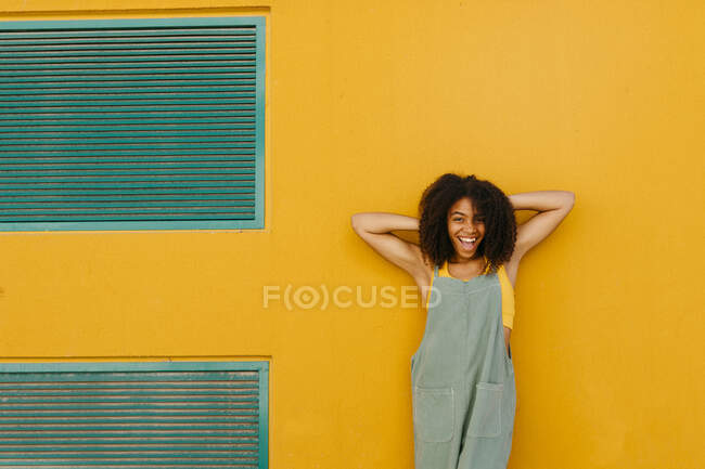 Ritratto di giovane donna felice che indossa una tuta davanti al muro giallo — Foto stock
