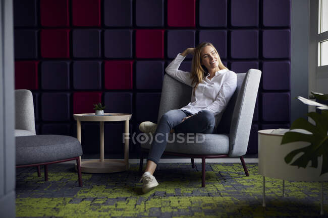 Donna sorridente seduta in poltrona nel salotto moderno — Foto stock