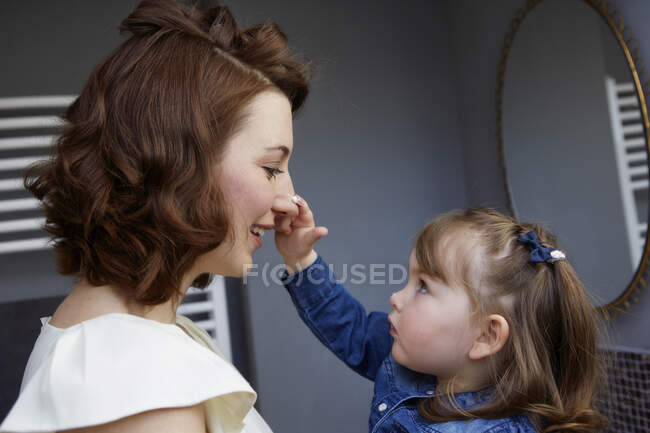 Petite fille appliquant de la crème sur le nez de sa mère — Photo de stock