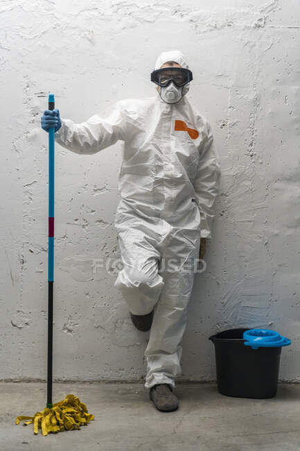 Mulher com equipamento de limpeza, vestindo roupas protetoras, encostada à parede — Fotografia de Stock