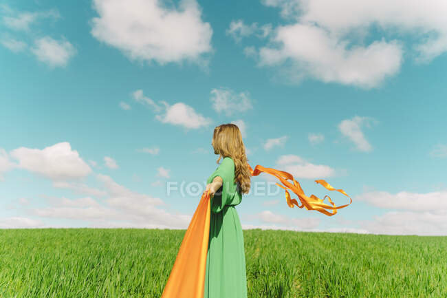 Jovem usando um vestido verde em um campo com fitas de sopro — Fotografia de Stock