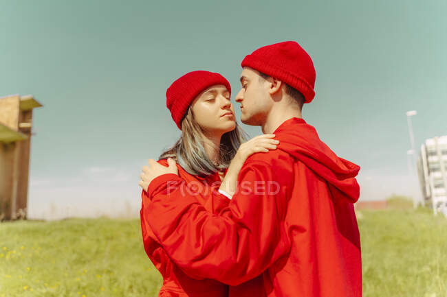 Young couple wearing red overalls and hats standing on a meadow — Stock Photo