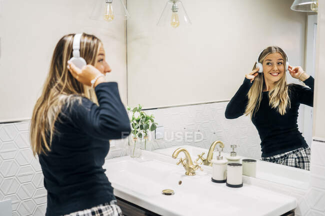 Image miroir de femme heureuse avec écouteurs dansant dans la salle de bain — Photo de stock